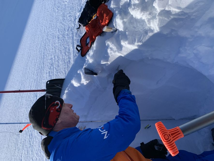 Man stands by a snowpack to measure the stability of the snow layers.