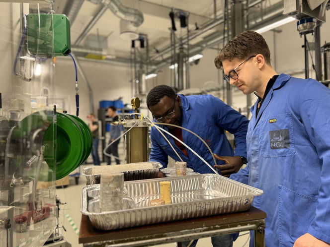 Fredrik and Jacob are wearing blue lab coats. In the background you can see typical lab equipment.